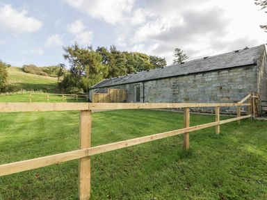 A stone barn with a slate roof surrounded by a grassy fenced yard at Lowdale Barns West in Sleights