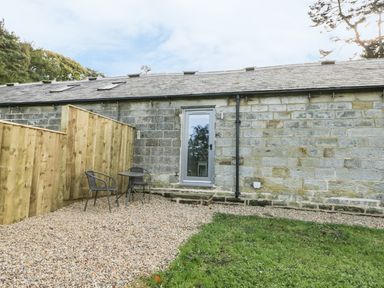 A stone building with a glass door a gravel patio area with two chairs and a table at Lowdale Barns West in Sleights