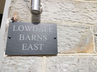 A stone wall with a rectangular plaque reading Lowdale Barns East and a metal light fixture above at Lowdale Barns East in Sleights