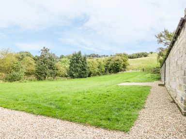 A grassy outdoor area with a gravel path and a stone wall alongside at Lowdale Barns East in Sleights
