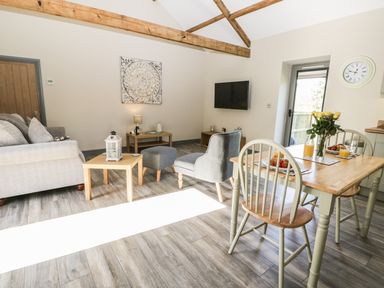 A living room with a gray sofa and armchair a wooden dining table with chairs and a flat screen tv on the wall at Lowdale Barns East Sleights
