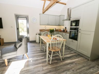 A kitchen and dining area with a wooden table set for two and a gray chair at Lowdale Barns East in Sleights