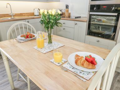 A kitchen with a wooden table set with plates of croissants and strawberries glasses of orange juice and a vase of white roses at Lowdale Barns East in Sleights