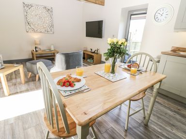 A dining table with croissants strawberries orange juice and flowers with chairs in a living room at Lowdale Barns East in Sleights