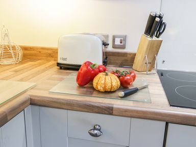 A kitchen countertop with a cutting board holding a red pepper a small pumpkin tomatoes and a knife alongside a knife block and a toaster at Lowdale Barns East in Sleights
