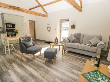 An open living area with a gray sofa, gray armchair, small table with a lantern, dining table with chairs and kitchen appliances at Lowdale Barns East in Sleights