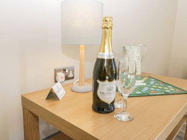 A wooden table with a bottle of prosecco two glasses a table lamp a metal jug and a scrabble game at Lowdale Barns East in Sleights