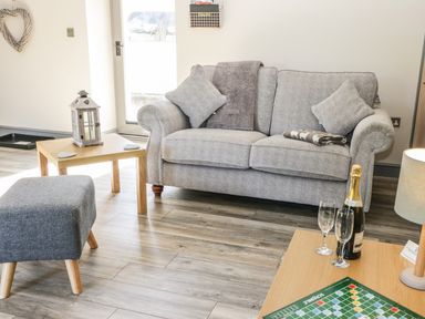 A living room with a gray sofa pillows blankets a wooden coffee table lantern ottoman champagne bottle glasses and a scrabble game at Lowdale Barns East in Sleights