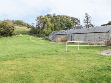 A grassy fenced yard with a stone building and trees in the background at Lowdale Barns East in Sleights