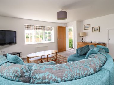 A living room with a curved teal patterned sofa a wooden coffee table a wall mounted TV and a wooden sideboard at 8 Pottergate Mews in Helmsley