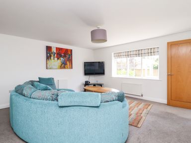 A living room with a curved blue sofa a wall mounted television a wooden door and a window with striped blinds at 8 Pottergate Mews Helmsley