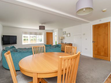 A living room with a round wooden dining table and chairs a teal sofa a wall-mounted television wooden doors and a sideboard at 8 Pottergate Mews in Helmsley