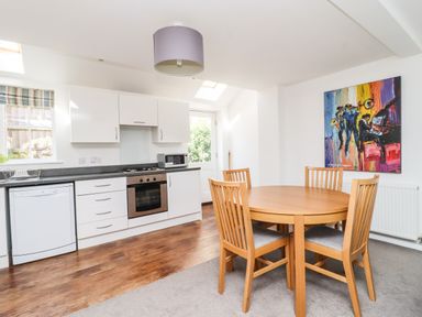 A kitchen and dining area with wooden table and chairs white cabinets and an oven at 8 Pottergate Mews in Helmsley
