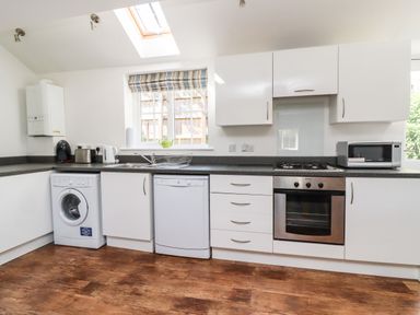 A kitchen with white cabinets a washing machine dishwasher oven microwave and a skylight at 8 Pottergate Mews Helmsley
