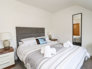 A bedroom with a double bed with pillows and folded towels bedside tables with lamps and a full length mirror on the wall at 8 Pottergate Mews in Helmsley