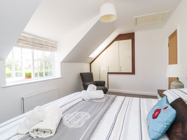 A bedroom with a bed with folded towels and pillows a window an armchair built-in cabinets and a lamp at 8 Pottergate Mews Helmsley