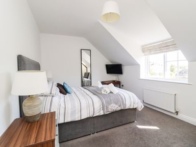 A bedroom with a double bed a bedside table with a lamp a wall-mounted TV a mirror and a window at 8 Pottergate Mews in Helmsley