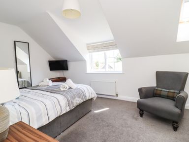 A bedroom with a bed, a gray armchair, a wall-mounted TV, a floor mirror, and a window at 8 Pottergate Mews in Helmsley