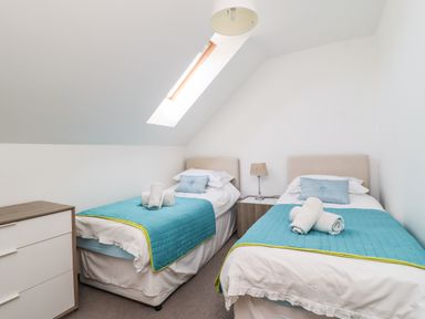 A bedroom with two single beds with blue covers and rolled towels a chest of drawers and a bedside table with a lamp at 8 Pottergate Mews in Helmsley