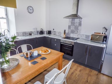 A kitchen with wooden dining table set with tea items and pastries and modern appliances at Harbour Beach at The Hideaway in Tenby
