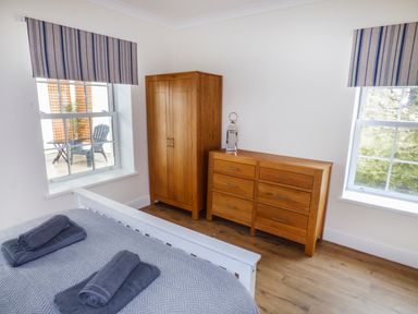 A bedroom with a white bed frame folded towels on the bed wooden wardrobe and chest of drawers under two windows at Harbour Beach at The Hideaway in Tenby