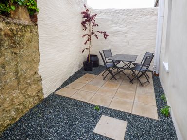 A small outdoor patio with a table, four chairs, potted plants, and gravel on the ground at Harbour Beach at The Hideaway in Tenby