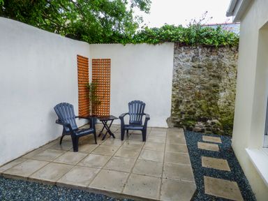 An outdoor patio area with two chairs a small table and a plant with stone and white walls at Harbour Beach at The Hideaway in Tenby