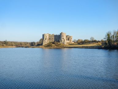 A large stone castle ruin on a grassy area surrounded by water under clear sky at Harbour Beach at The Hideaway in Tenby