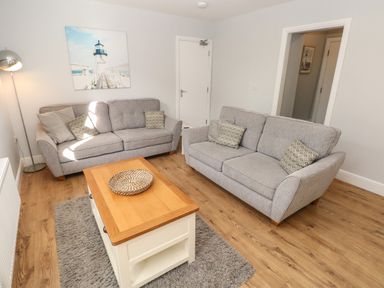 A living room with two grey sofas a wooden coffee table a floor lamp and a wall picture of a lighthouse at Harbour Beach at The Hideaway in Tenby