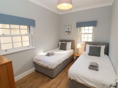 A bedroom with two single beds a wooden side table with a lamp and two windows at Harbour Beach at The Hideaway in Tenby