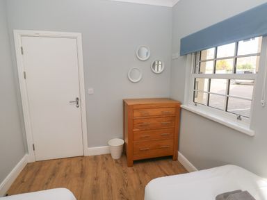 A bedroom corner with a wooden chest of drawers a white door a window with a blue blind and a white trash bin at Harbour Beach at The Hideaway in Tenby
