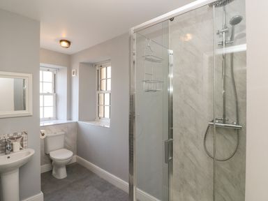 A bathroom with a shower enclosure a toilet a sink and two windows at Harbour Beach at The Hideaway in Tenby