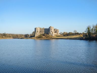 A stone castle on land surrounded by water and trees at North Beach at The Hideaway in Tenby