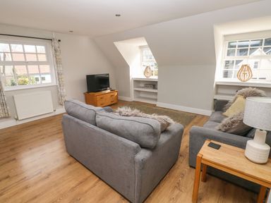 A living room with two grey sofas a wooden TV stand with a television and wooden side table with a lamp at North Beach at The Hideaway in Tenby