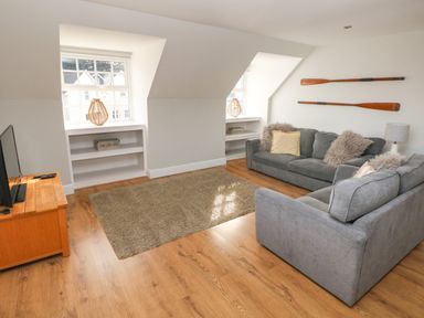 A living room with two gray sofas a wooden TV stand with a television two windows with built in shelves and wooden paddles on the wall at North Beach at The Hideaway in Tenby
