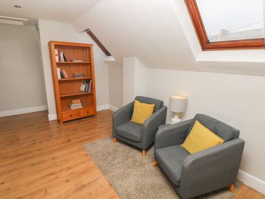 A seating area with two gray armchairs with yellow cushions a lamp and a wooden bookshelf in a room with wooden flooring and skylights at North Beach at The Hideaway in Tenby