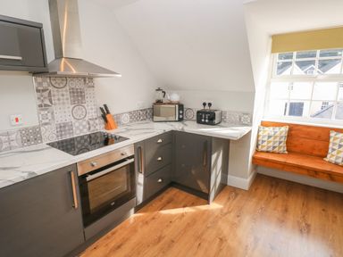 A kitchen corner with a stove oven microwave toaster and a wooden bench with pillows by a window at North Beach at The Hideaway in Tenby
