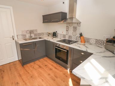 A kitchen with gray cabinets white marble countertops and patterned tile backsplash at North Beach at The Hideaway in Tenby