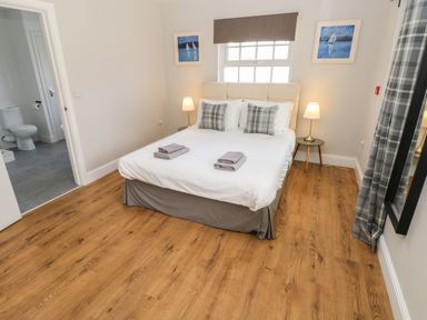 A bedroom with a double bed bedside tables lamps window and an open door leading to a bathroom at North Beach at The Hideaway in Tenby