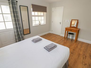 A bedroom with a bed with folded towels a full length mirror a window with a blind and a wooden dressing table at North Beach at The Hideaway in Tenby
