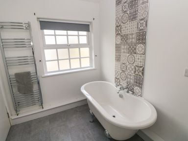 A bathroom with a standalone bathtub a patterned tile wall window with a blind and a towel rack at North Beach at The Hideaway in Tenby