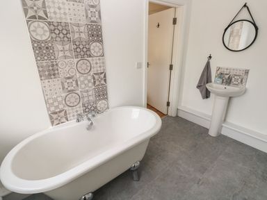 A bathroom with a clawfoot bathtub pedestal sink circular mirror and patterned tile accents at North Beach at The Hideaway in Tenby