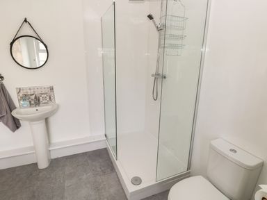 A bathroom with a pedestal sink a round mirror a glass shower enclosure and a toilet at North Beach at The Hideaway in Tenby
