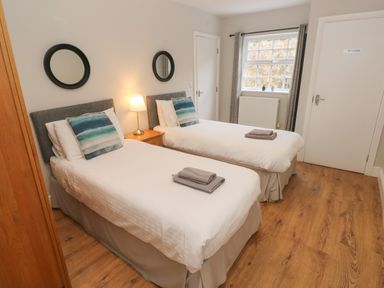 A bedroom with two single beds a wooden nightstand lamp two round mirrors window with curtains and wood floor at North Beach at The Hideaway in Tenby