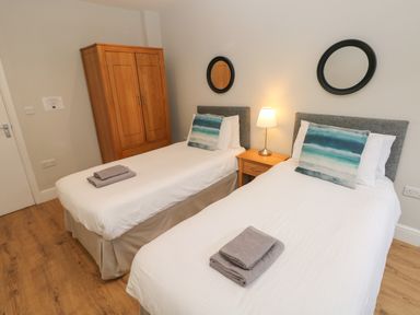 A bedroom with two single beds each with folded towels bedside table with lamp and wooden wardrobe at North Beach at The Hideaway in Tenby