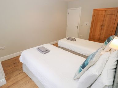 A bedroom with two single beds with white bedding gray towels on top a wooden wardrobe and a door at North Beach at The Hideaway in Tenby