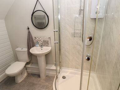 A bathroom with a toilet sink round mirror shower enclosure and towel at North Beach at The Hideaway in Tenby