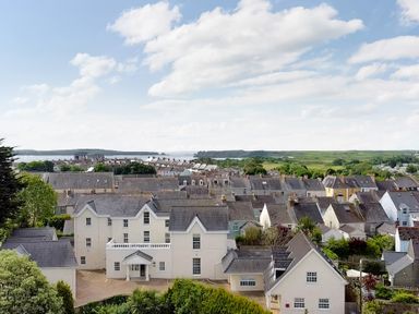 A view of residential houses with pitched roofs and greenery with hills and water in the background at North Beach at The Hideaway in Tenby