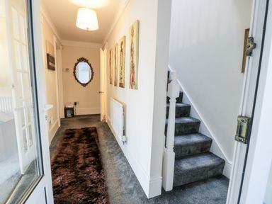 A hallway with carpeted stairs a brown rug a wall mirror and framed pictures at 11 Glyn Garth Mews in Llandegfan near Beaumaris