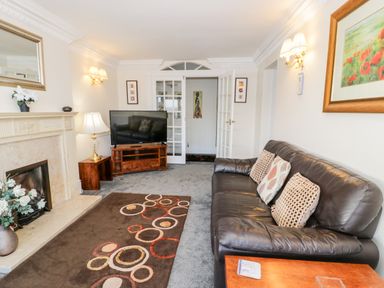 A living room with a black leather sofa a fireplace a television on a wooden stand and a patterned rug at 11 Glyn Garth Mews in Llandegfan near Beaumaris